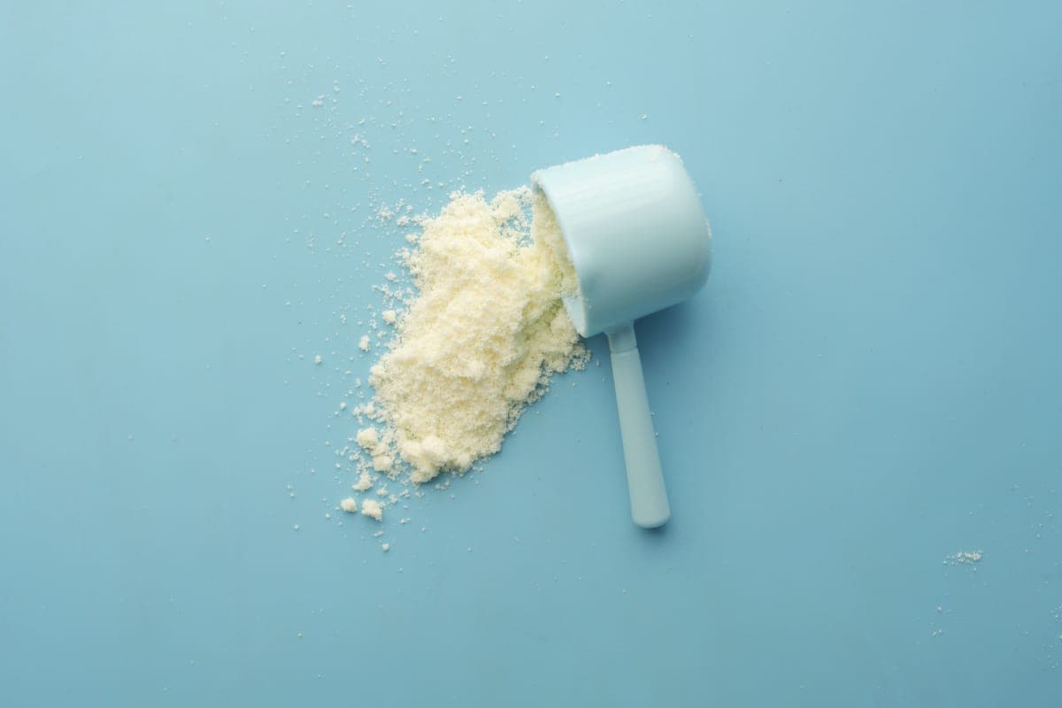 Illustrative stock photo: protein powder spilled from a scoop on a blue background