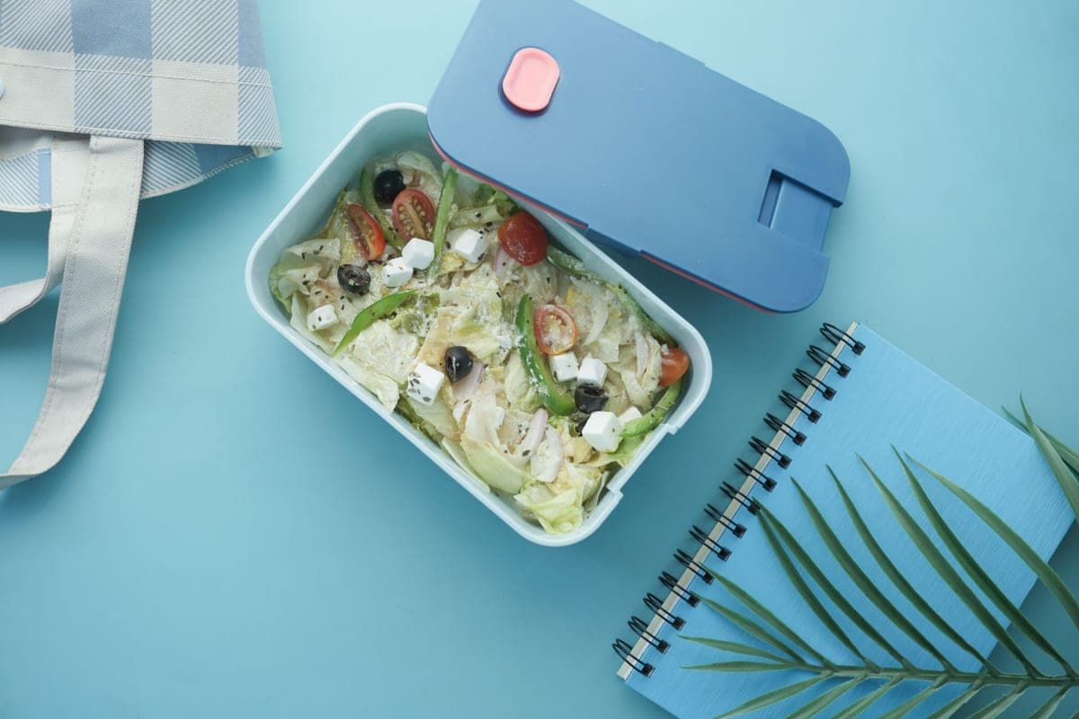 Illustrative stock photo: a salad lunch box beside a notebook on a blue background, seen from above