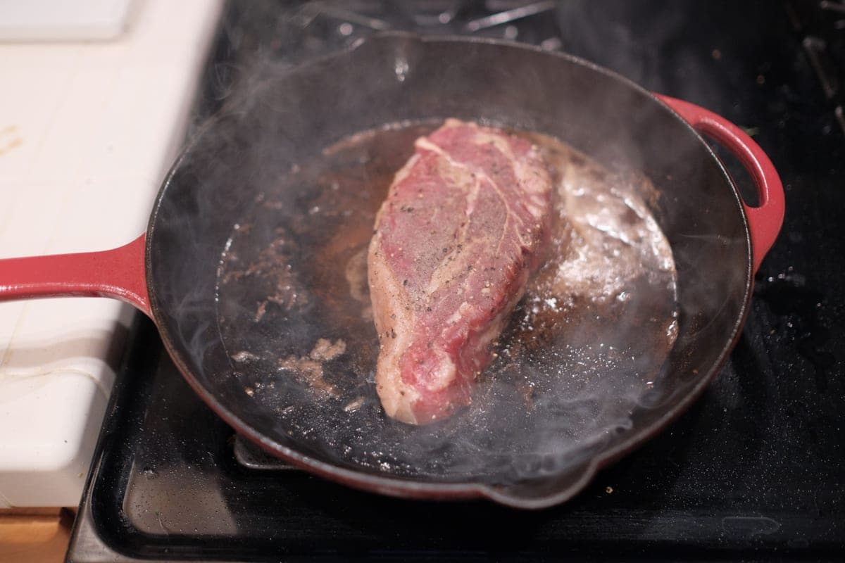Illustrative stock photo: a steak sizzling in a cast iron skillet on a stove