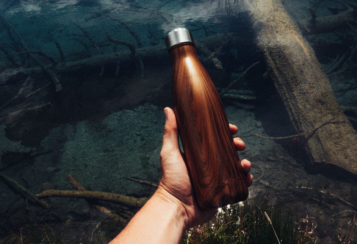 Illustrative stock photo: a hand holding a stainless steel water bottle over a stream