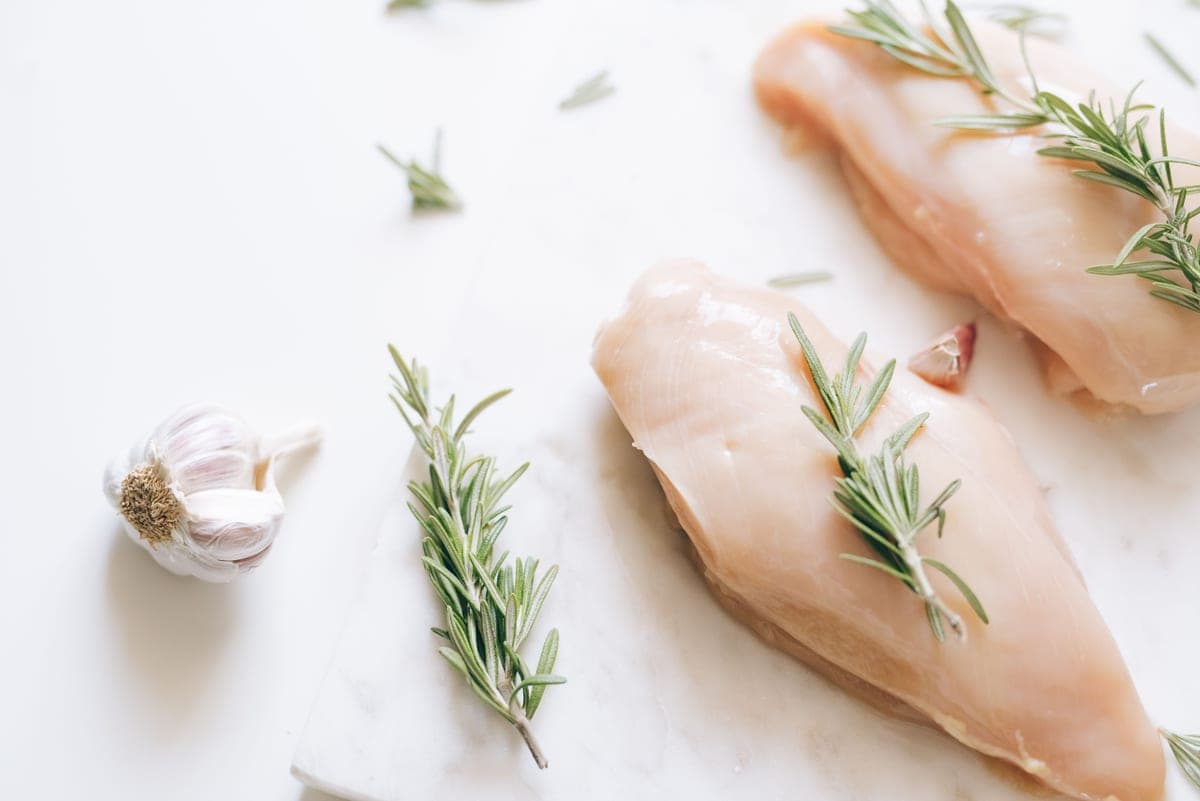 Illustrative stock photo: raw chicken breasts with rosemary and garlic on a white surface