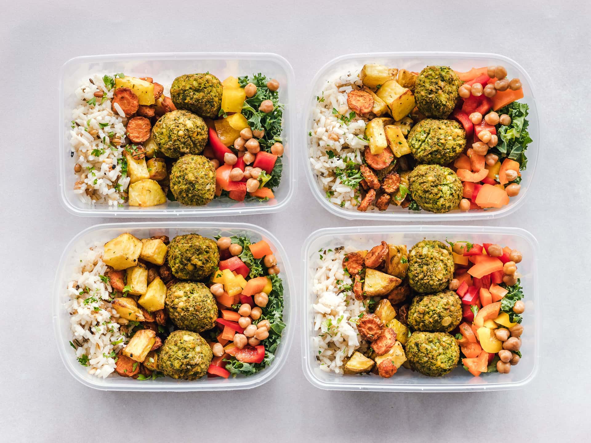 Meal prep containers filled with falafel, chickpeas, rice and vegetables, seen from above
