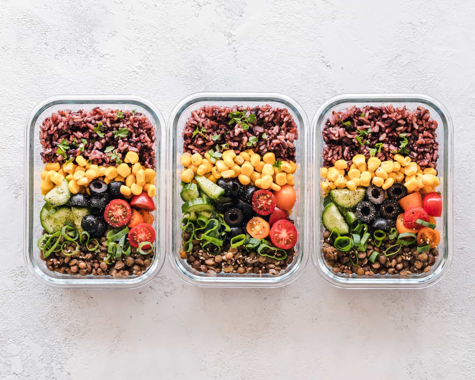 Three glass containers of corn, olives, tomatoes and lentils laid out on a table