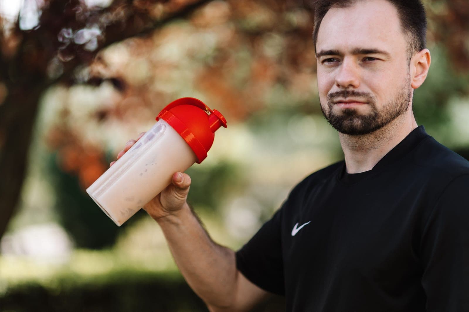 A man holding a shaker bottle with a red lid outdoors